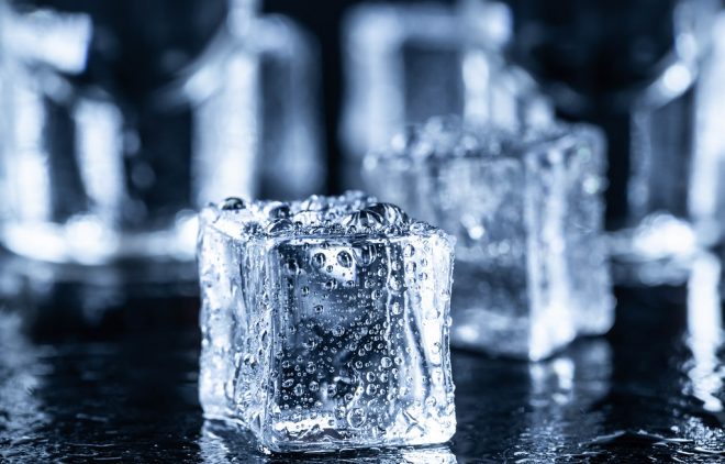 Ice cubes with water drops and vodka glasses in the background
